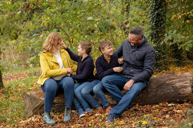 Claire and her family sitting together on a log among autumn leaves