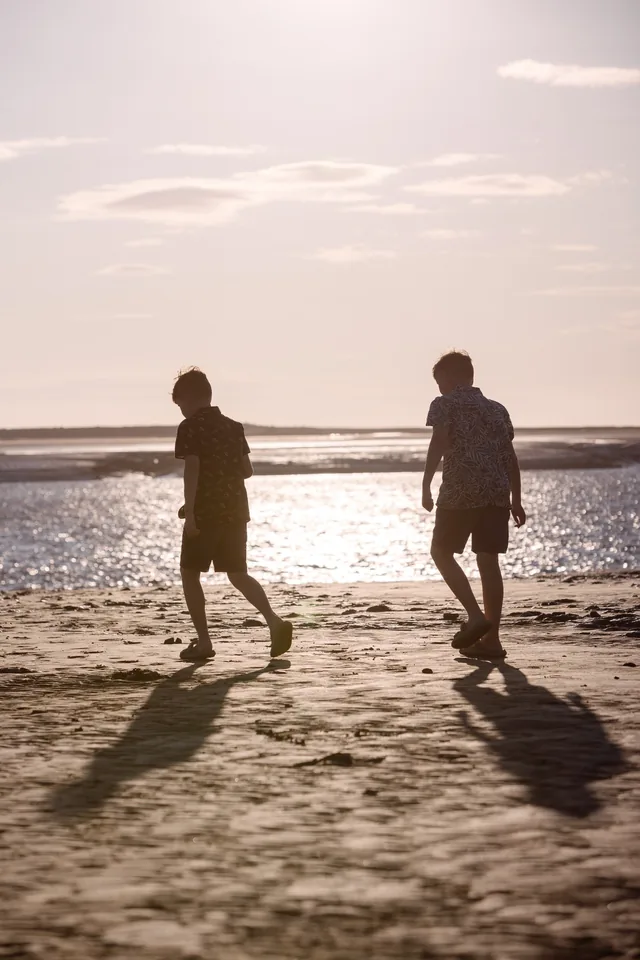 Claire’s two boys silhouetted on the beach beneath a soft pink sunset sky