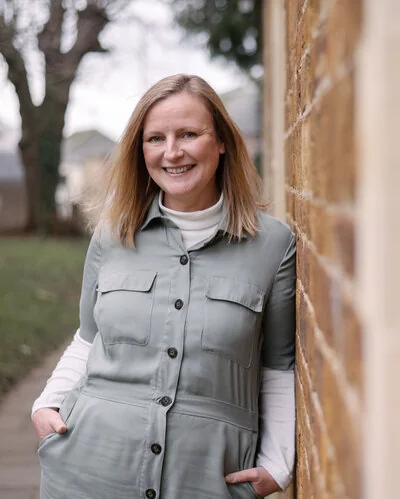 Claire smiling in a green jumpsuit beside a brick wall