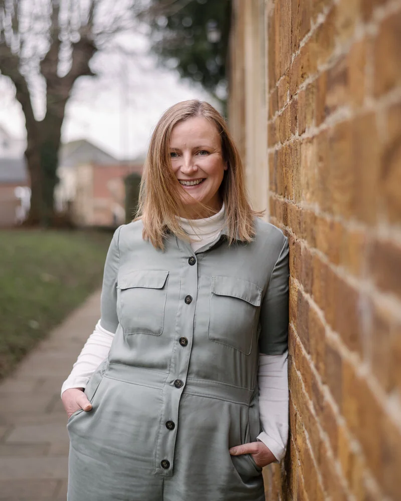 Claire smiling in a green jumpsuit beside a brick wall