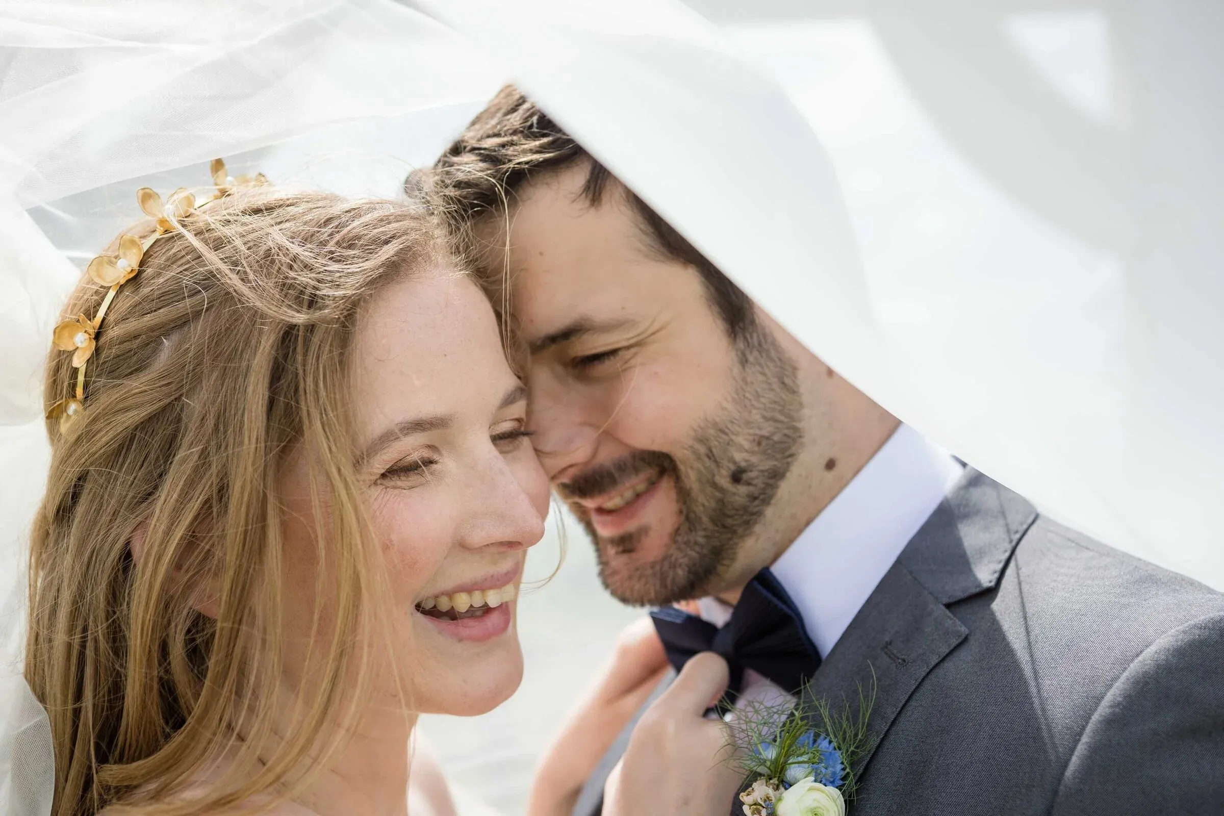 A wedding couple laughing together beneath a white veil