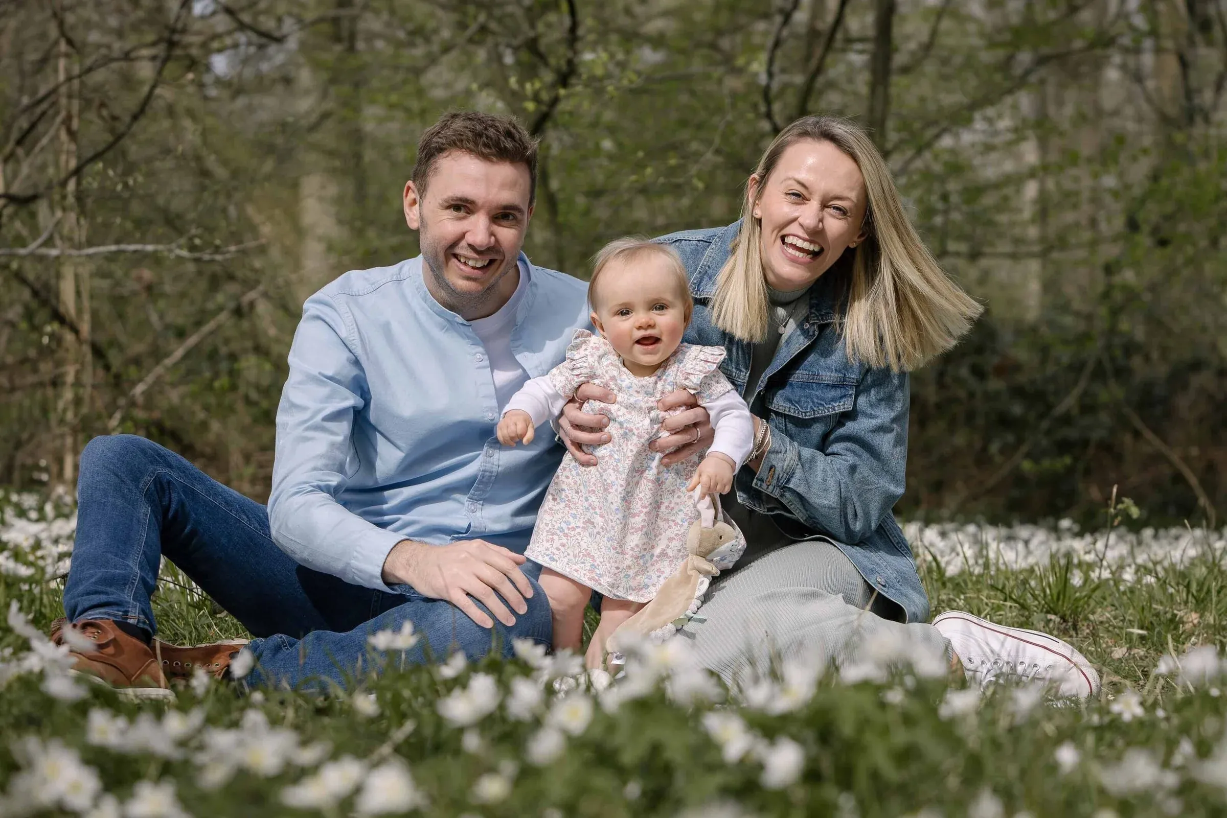 Parents laughing with their baby among white woodland flowers