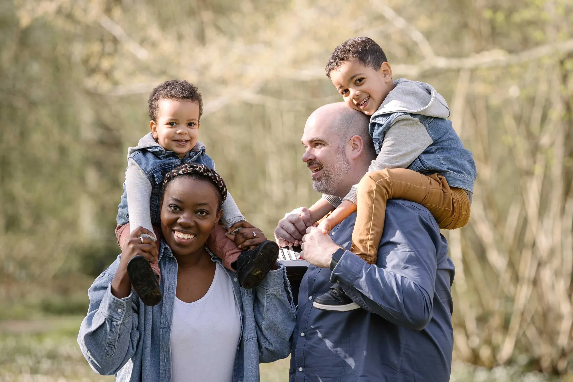 Two parents carrying their smiling children on their shoulders outdoors