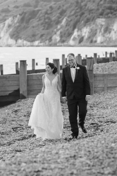 Black and white portrait of a wedding couple walking on a pebble beach