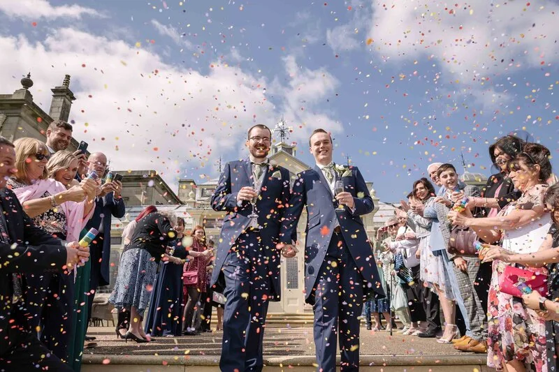 A newly married couple walking through colourful confetti and cheering guests