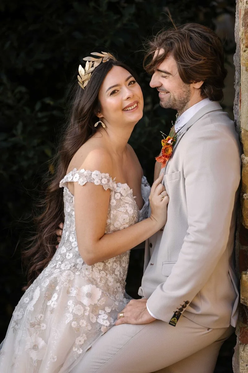 A wedding couple laughing together beside a garden wall