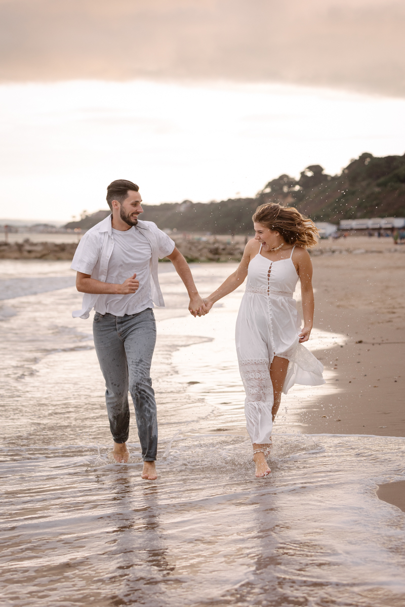 A couple running playfully through the shoreline on a beach in Dorset