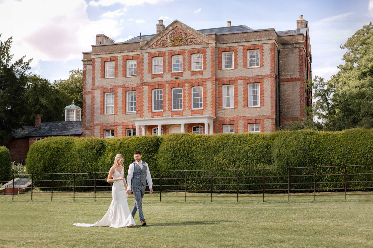 Newlyweds strolling hand-in-hand with Ardington House in the background.