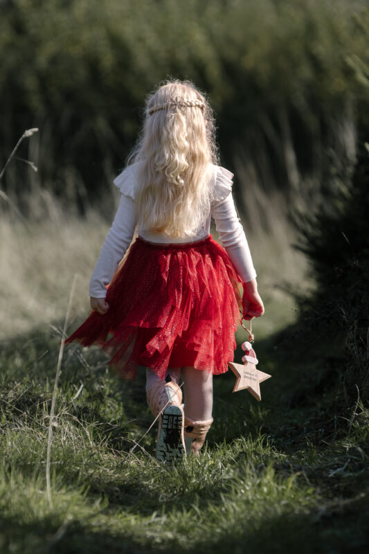 A little girl waking through christmas trees in Northamptonshire holding a decoration